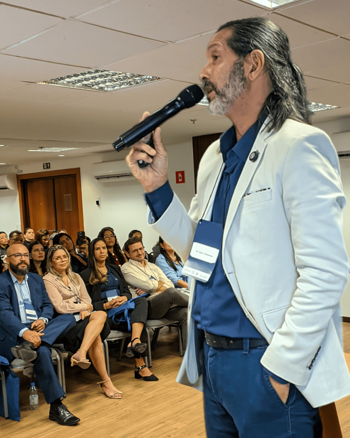 Prof. Charles Albuquerque em retrato de terno, braços abertos